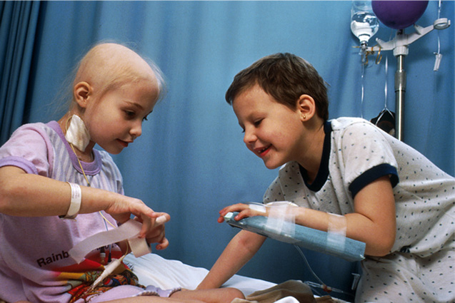 two child cancer patients play in hospital bed